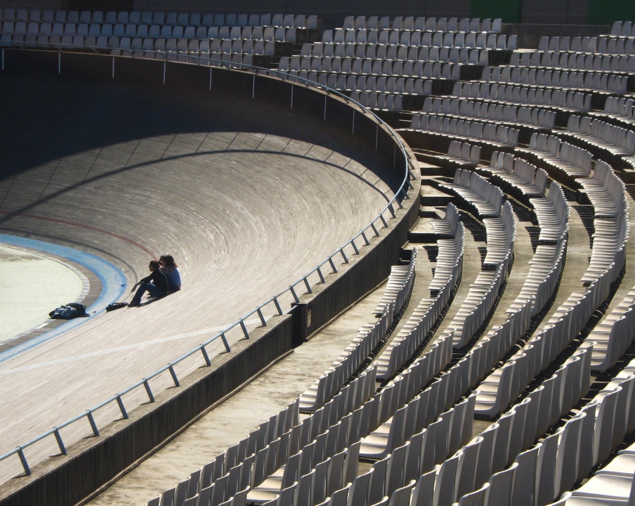 Curva peraltada del Velòdrom d'Horta, en Barcelona, vista desde la grada vacía, con dos personas sentadas sobre la pista