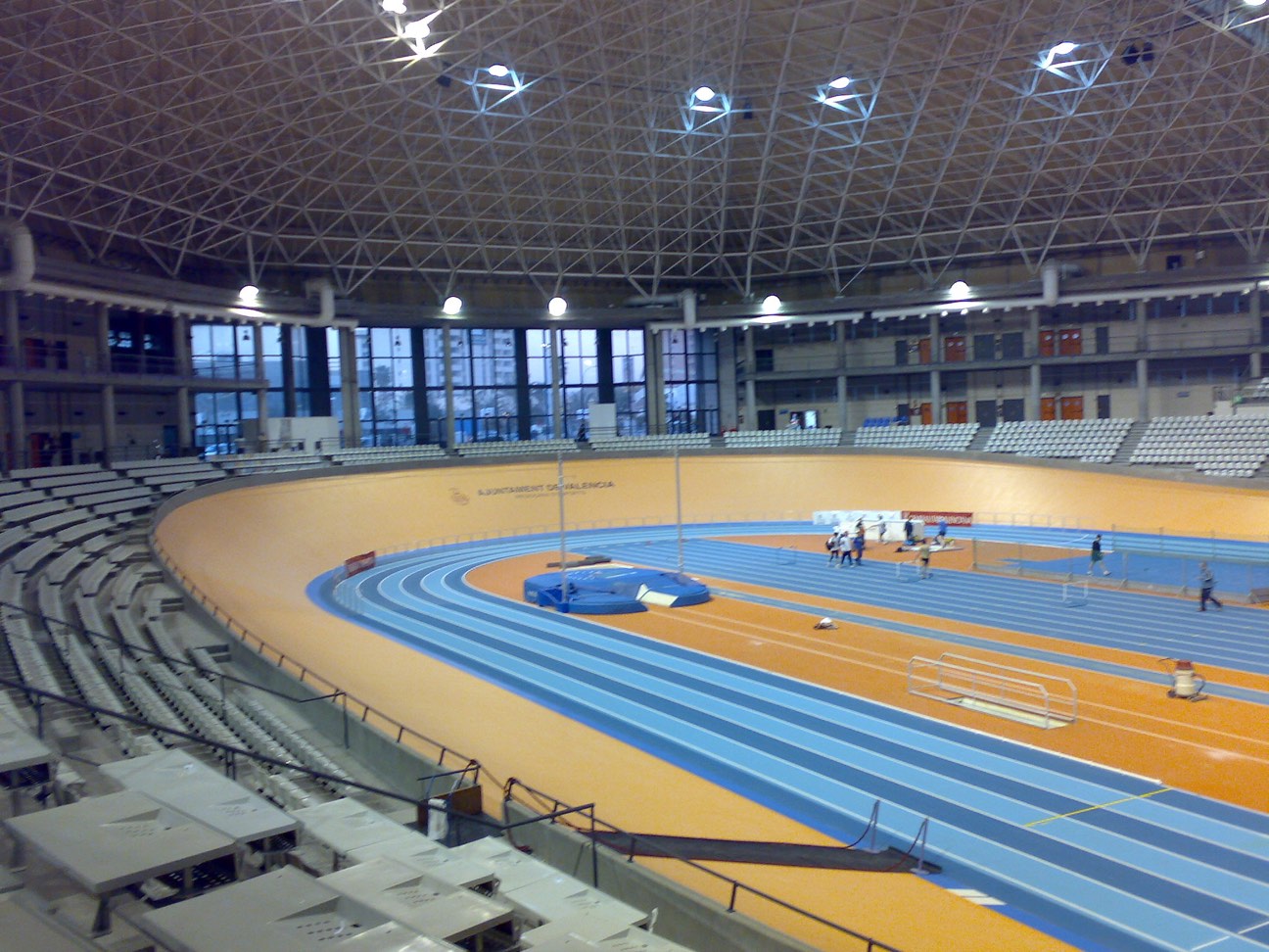 Interior del Palau Velòdrom Lluís Puig, con la pista peraltada de color anaranjado alrededor de una pista de atletismo azul, bajo una cubierta de estructura metálica