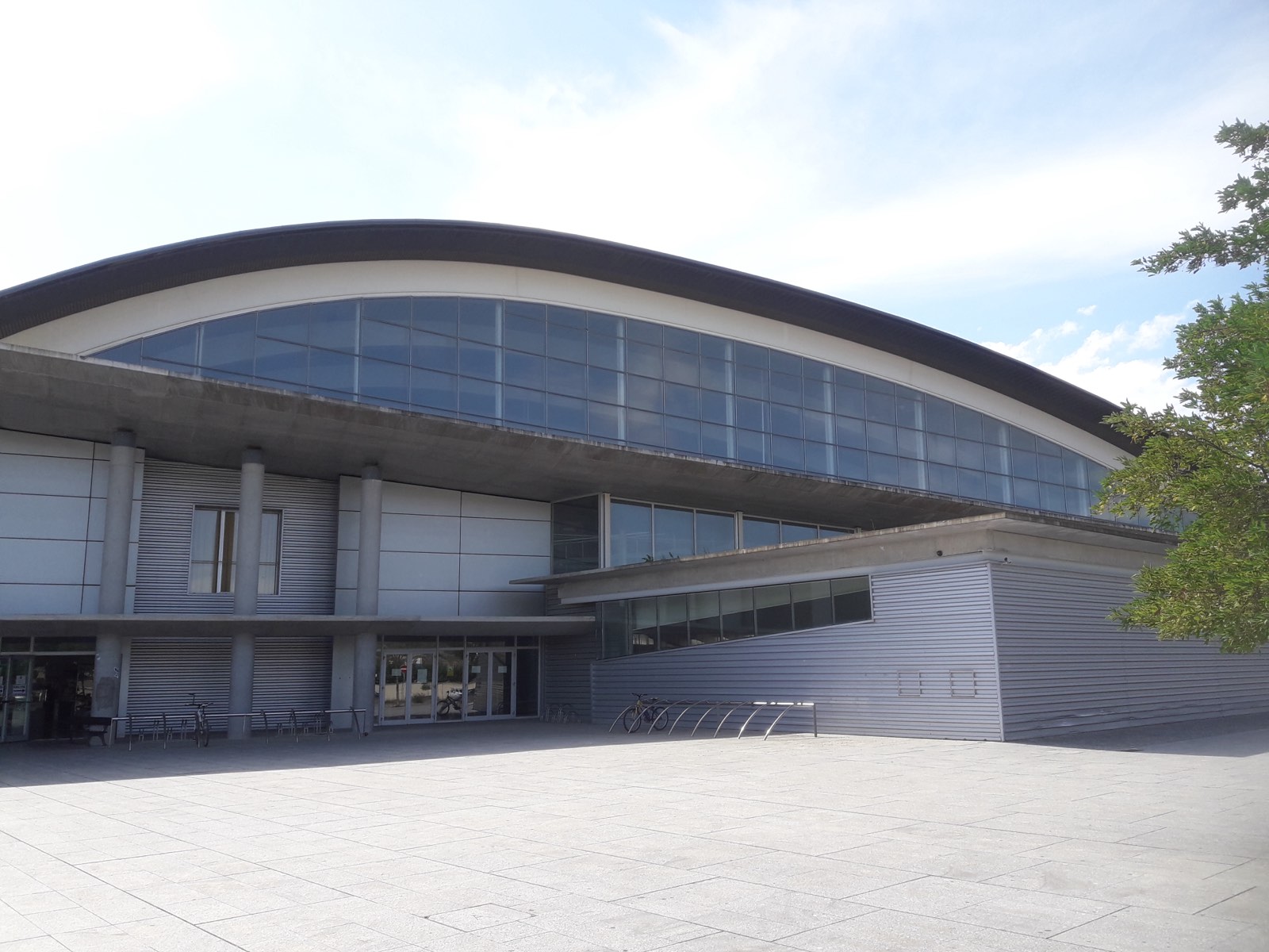 Fachada acristalada de la ciudad deportiva de Tafalla, con la cubierta curva del velódromo Miguel Induráin