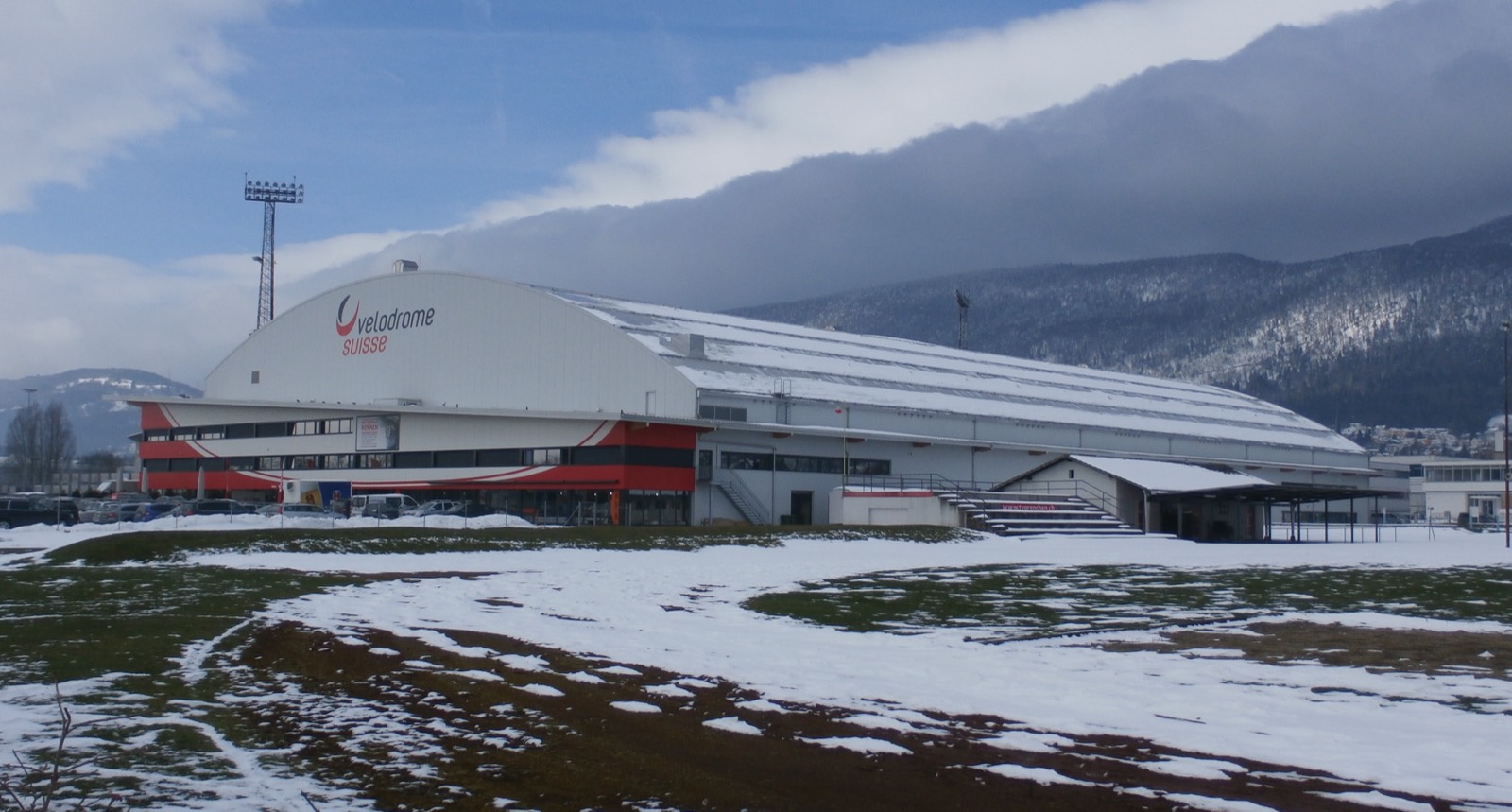 Edificio del Velodrome Suisse de Grenchen, con nieve en el terreno de delante y las montañas del Jura detrás